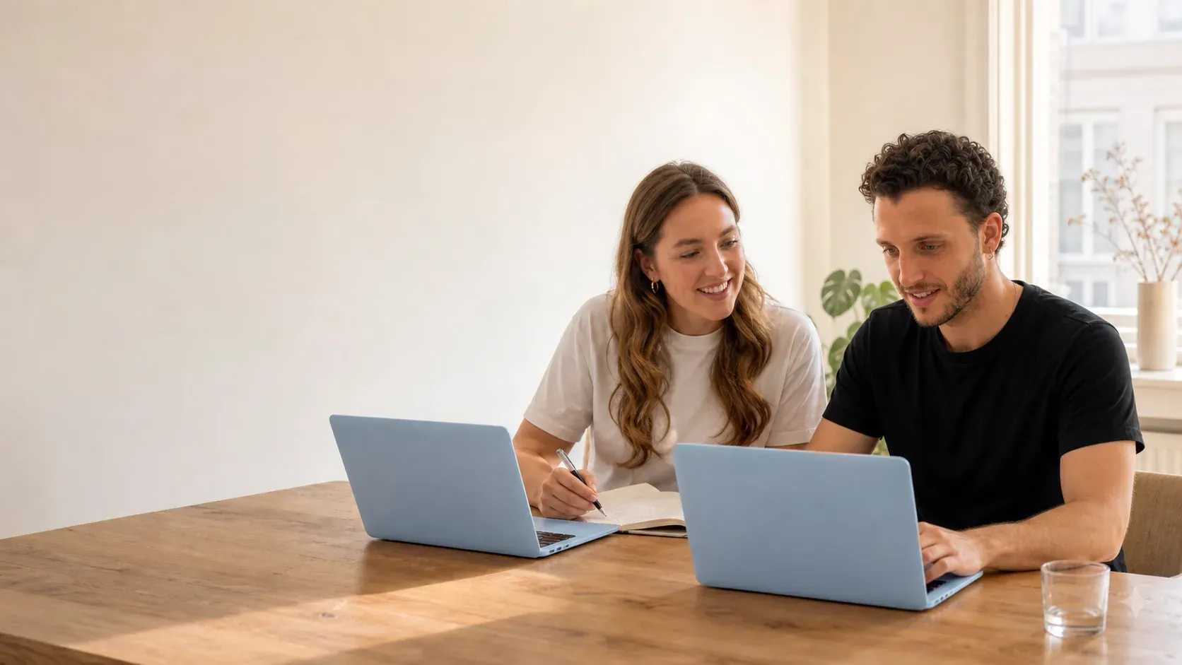Two people working side by side on laptops at a wooden table