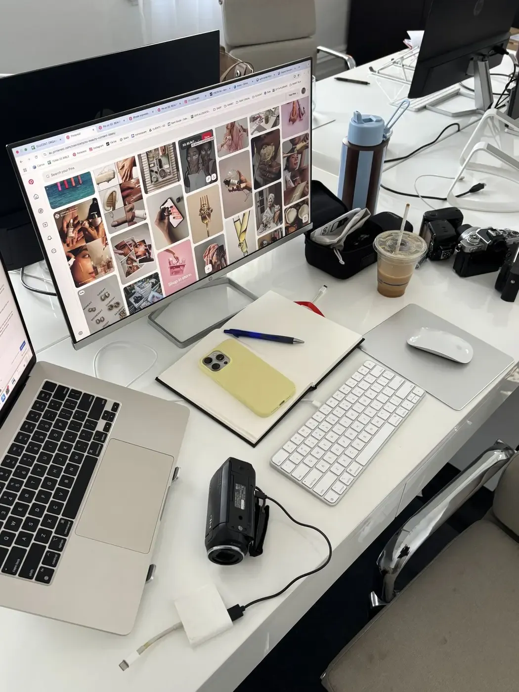 A desk with a monitor showing a grid of moodboard images, a laptop and two cameras